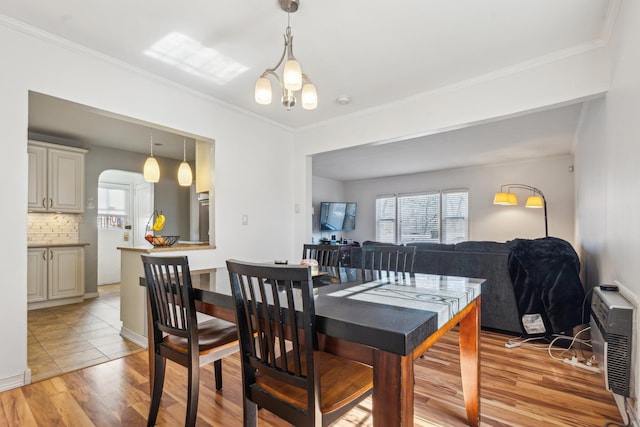 dining space featuring crown molding, light wood-style flooring, and arched walkways