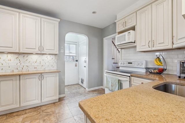 kitchen featuring baseboards, decorative backsplash, arched walkways, white appliances, and a sink