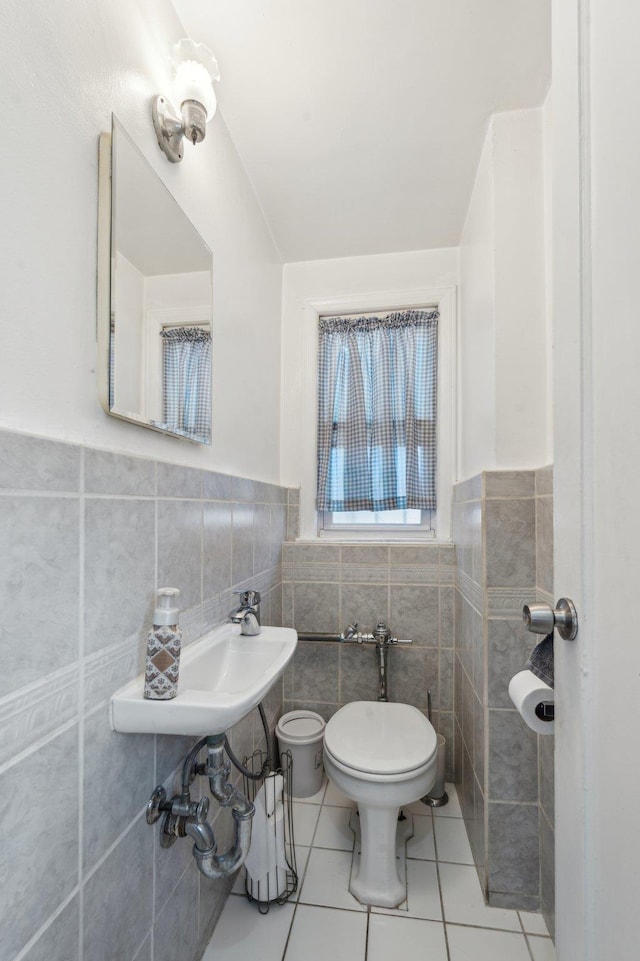 bathroom with tile patterned floors, a wainscoted wall, toilet, a sink, and tile walls