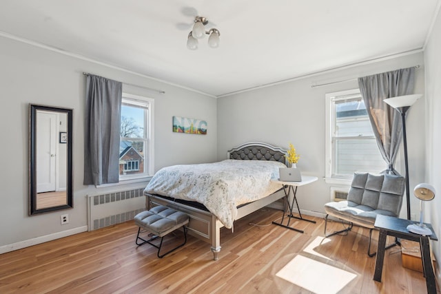 bedroom featuring light wood finished floors, multiple windows, radiator, and crown molding