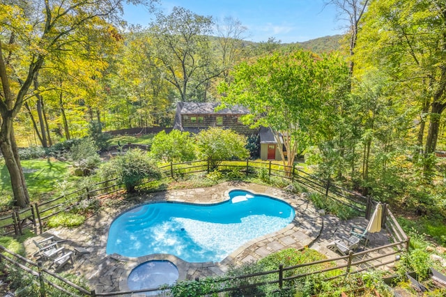 view of swimming pool featuring a view of trees, a pool with connected hot tub, and fence