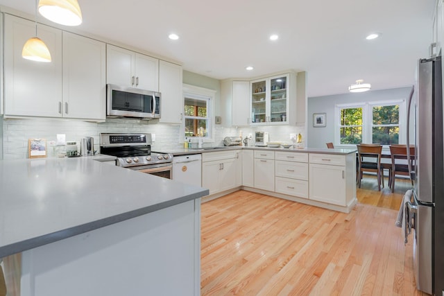 kitchen featuring a peninsula, white cabinets, light wood-style floors, appliances with stainless steel finishes, and tasteful backsplash