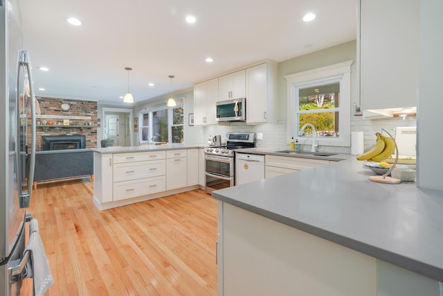 kitchen with light wood finished floors, a peninsula, stainless steel appliances, white cabinetry, and a sink