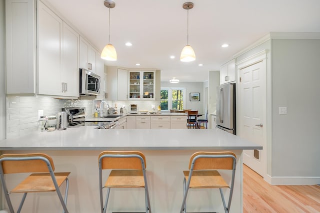 kitchen featuring light wood finished floors, backsplash, stainless steel appliances, a peninsula, and light countertops