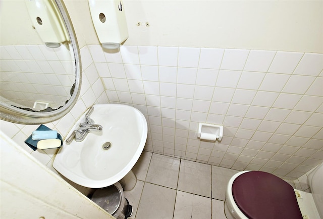 half bathroom with toilet, tile patterned flooring, a sink, and tile walls