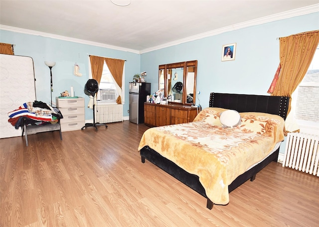 bedroom with ornamental molding, radiator heating unit, wood finished floors, and freestanding refrigerator