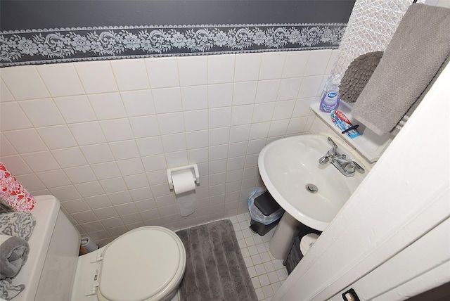 bathroom featuring toilet, tile walls, a sink, and tile patterned floors