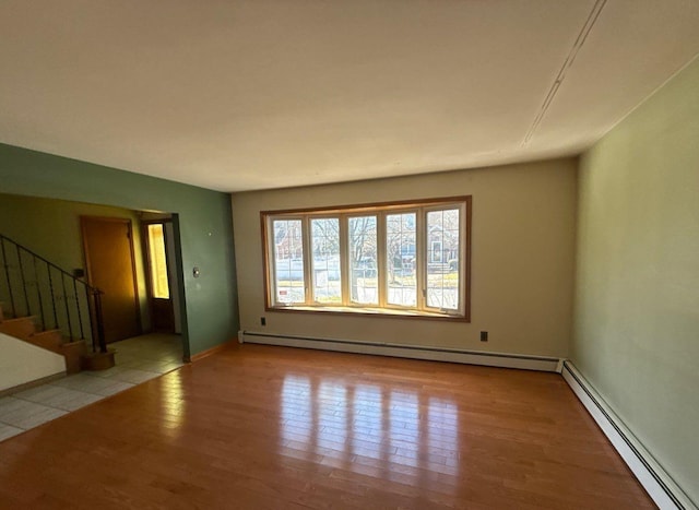 unfurnished room featuring stairs, a baseboard heating unit, and wood finished floors