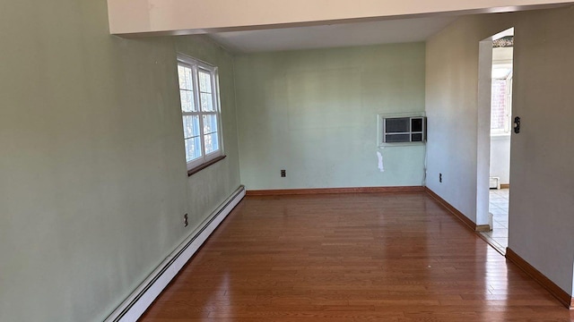 empty room with a baseboard heating unit, a wall mounted AC, baseboards, and wood finished floors