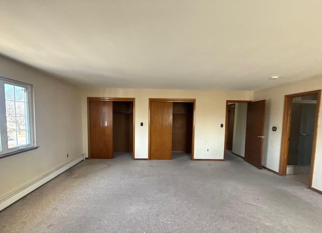 unfurnished bedroom featuring light carpet, baseboard heating, two closets, and baseboards