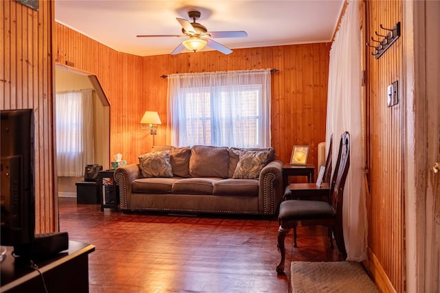 living area with a ceiling fan and wood walls