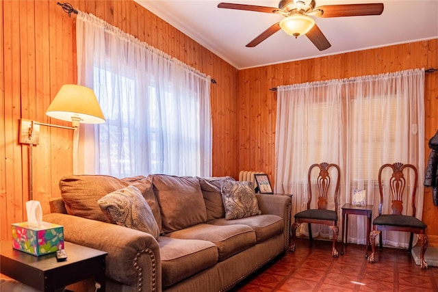 living room featuring wood walls, ceiling fan, and crown molding