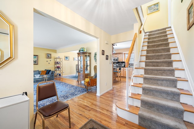 foyer entrance featuring light wood-type flooring, stairs, baseboards, and crown molding