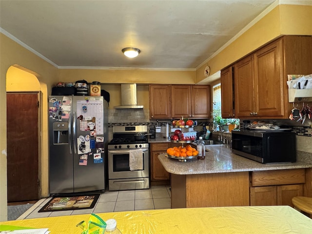 kitchen featuring brown cabinets, stainless steel appliances, arched walkways, light tile patterned flooring, and wall chimney range hood