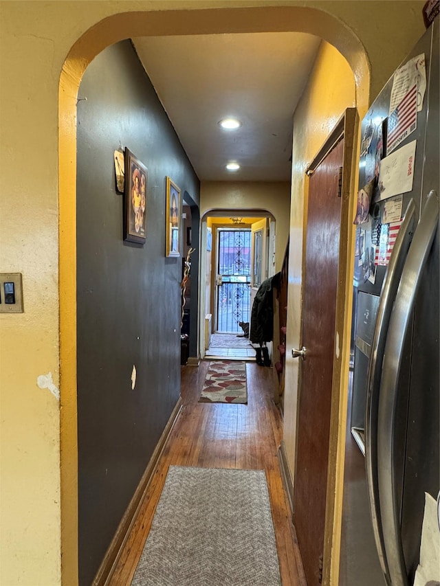 corridor with arched walkways, baseboards, and wood finished floors