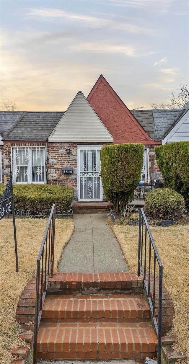 view of front of house featuring brick siding, a front lawn, and roof with shingles