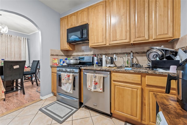 kitchen with appliances with stainless steel finishes, arched walkways, light tile patterned flooring, and decorative backsplash