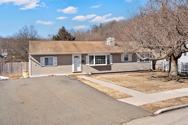 single story home with aphalt driveway, a chimney, and fence