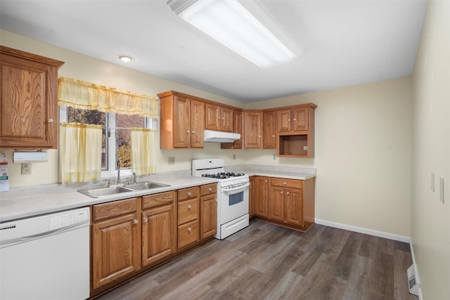 kitchen with white appliances, dark wood-style floors, baseboards, a sink, and under cabinet range hood