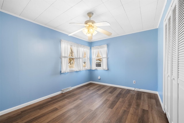 empty room featuring a ceiling fan, baseboards, visible vents, dark wood finished floors, and ornamental molding