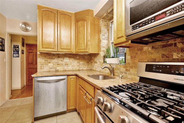 kitchen with light tile patterned floors, decorative backsplash, appliances with stainless steel finishes, light stone counters, and a sink