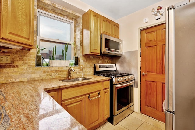 kitchen with decorative backsplash, appliances with stainless steel finishes, light stone counters, a sink, and light tile patterned flooring