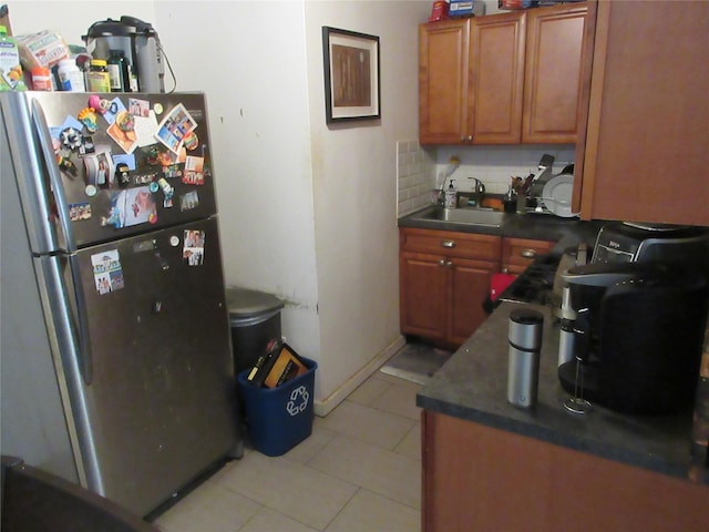 kitchen featuring decorative backsplash, dark countertops, freestanding refrigerator, a sink, and light tile patterned flooring