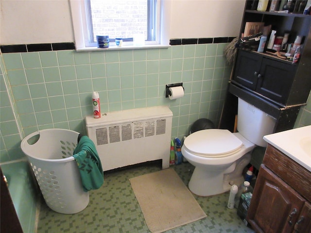 bathroom with wainscoting, radiator, toilet, vanity, and tile walls