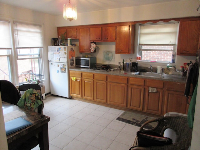 kitchen with brown cabinets, decorative light fixtures, stainless steel appliances, a sink, and light tile patterned flooring