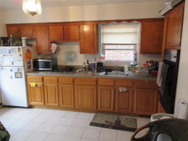 kitchen with stainless steel appliances, brown cabinetry, a sink, and light tile patterned floors