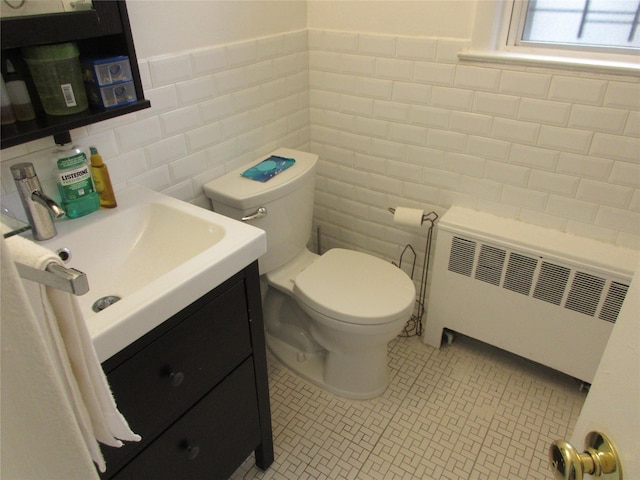 half bathroom with toilet, vanity, tile walls, tile patterned floors, and radiator