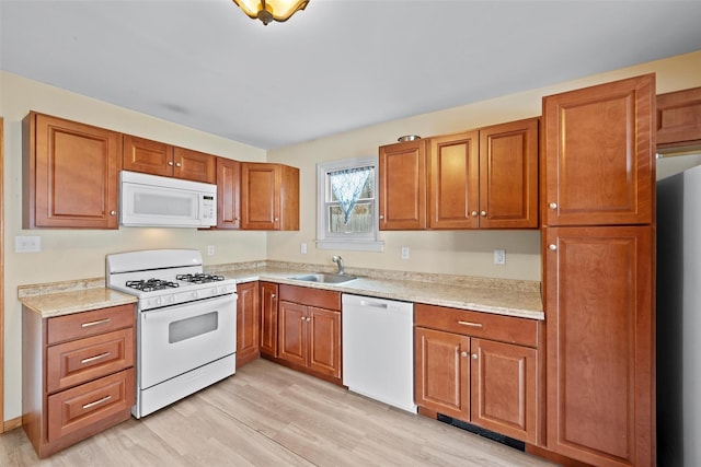 kitchen with white appliances, a sink, light countertops, light wood-type flooring, and brown cabinets