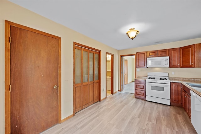 kitchen with baseboards, light countertops, white appliances, and light wood-style floors