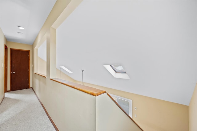 corridor featuring lofted ceiling with skylight, carpet flooring, an upstairs landing, and baseboards