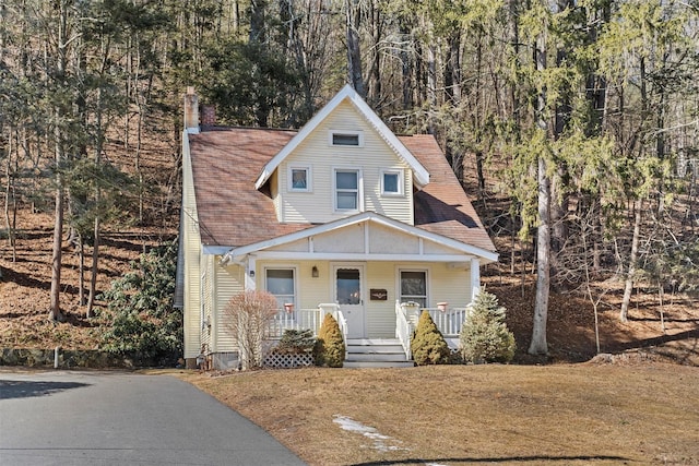 view of front of house featuring covered porch, a front yard, and roof with shingles