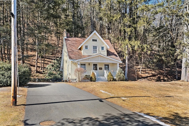 view of front of house with covered porch, a front lawn, and a shingled roof