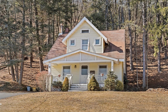 view of front of house featuring a front lawn, covered porch, and a shingled roof