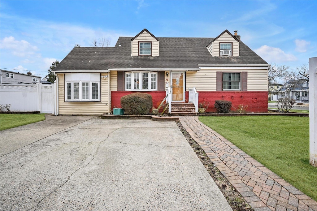 cape cod-style house featuring driveway, roof with shingles, fence, a front yard, and brick siding