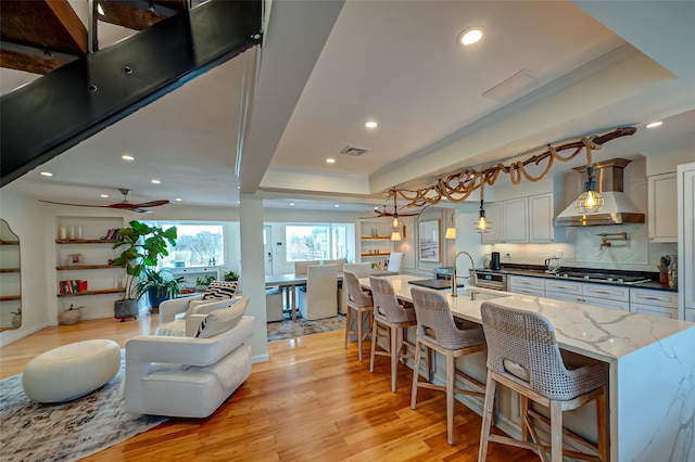 kitchen featuring visible vents, stovetop, a raised ceiling, wall chimney exhaust hood, and open floor plan