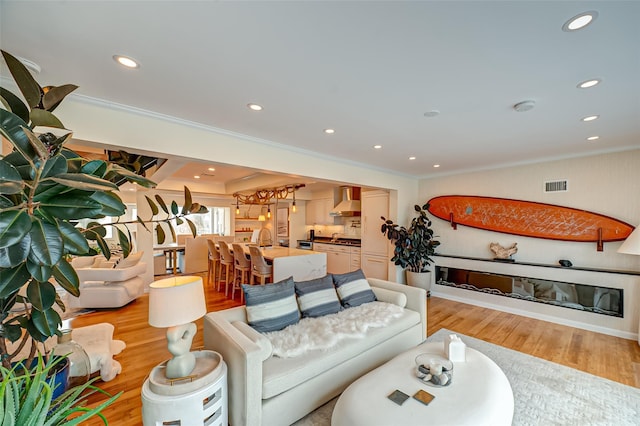 living area featuring visible vents, recessed lighting, light wood-style floors, and ornamental molding