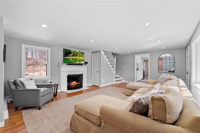 living area with recessed lighting, a fireplace with flush hearth, stairs, baseboard heating, and light wood finished floors