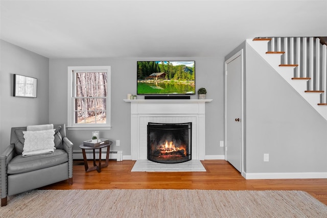 living room with stairs, wood finished floors, a baseboard radiator, and a fireplace