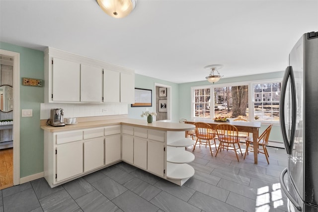 kitchen with tasteful backsplash, white cabinets, freestanding refrigerator, a peninsula, and light countertops