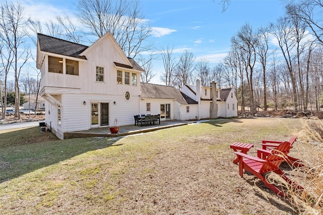 rear view of property featuring a shingled roof, board and batten siding, a patio area, and a lawn