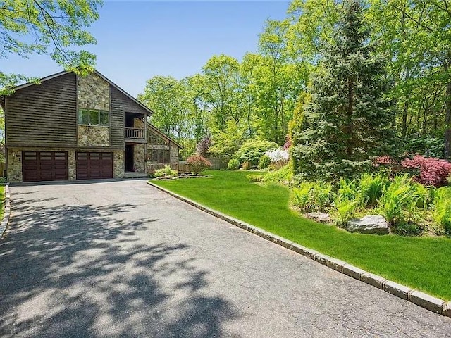 view of front of property with an attached garage, stone siding, a front lawn, and aphalt driveway