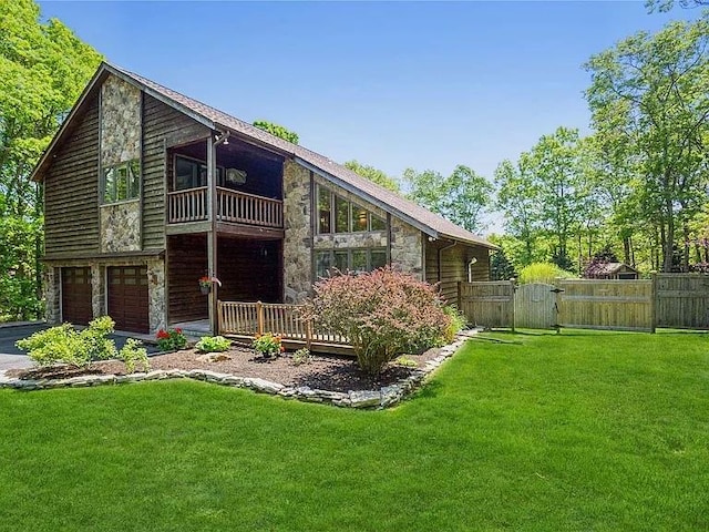 back of property with a balcony, fence, stone siding, a lawn, and a gate