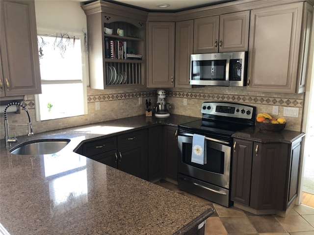 kitchen with stainless steel appliances, a sink, decorative backsplash, open shelves, and dark stone countertops