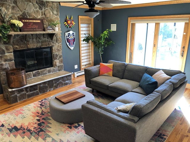 living area with ceiling fan, a baseboard heating unit, wood finished floors, and a stone fireplace