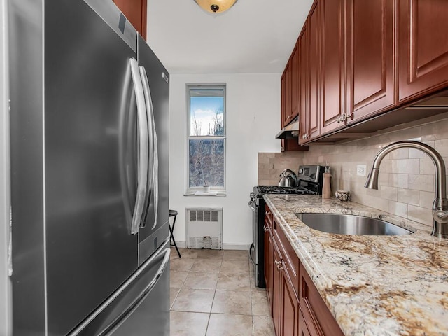 kitchen featuring tasteful backsplash, appliances with stainless steel finishes, light stone counters, under cabinet range hood, and a sink