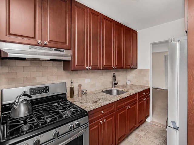 kitchen with light stone counters, refrigerator, under cabinet range hood, a sink, and stainless steel range with gas stovetop